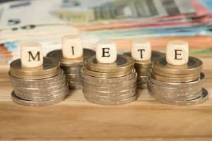 Nahaufnahme gestapelter Euromünzen mit Holzbuchstabenwürfeln die MIETE schreiben unscharfe Banknoten im Hintergrund