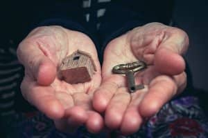 Close-up bird's eye view of a small wooden house model and antique key in open hands