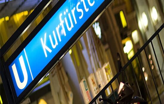 U-Bahnstation Kurfürstendamm bei Nacht schräg frontal mit Leuchtschild und Geländer im Vordergrund