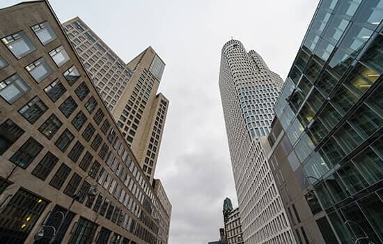 Blick von unten auf modernes Hochhausensemble mit rundem Fassadenturm und Glasfronten bei bewölktem Himmel