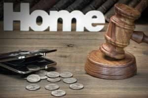 Auction hammer next to opened purse with scattered coins in front of white Home lettering on wooden table