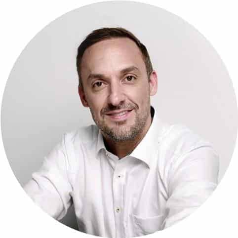 Porträtfoto eines lächelnden Mannes im weißen Hemd vor hellem, kreisrund beschnittenem Hintergrund