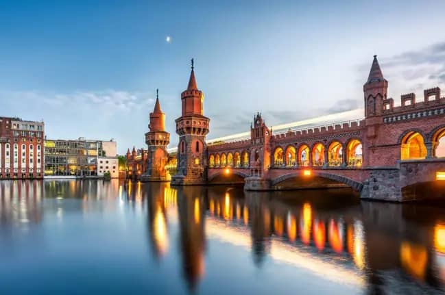 Abendliche Ansicht der historischen Oberbaumbrücke mit roten Backsteintürmen und Lichterspiegelung auf der Spree