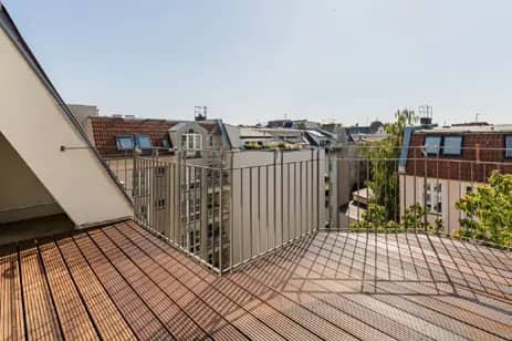Balkon mit Holzlattenboden in Dachgeschosswohnung Blick über umliegende Dachterrassen und Mehrfamilienhäuser