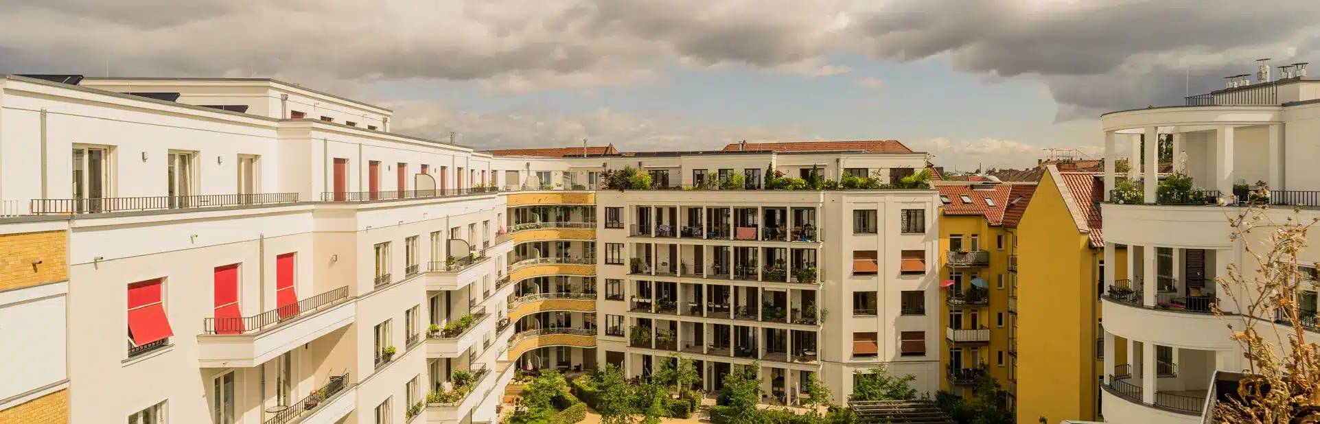 Vogelperspektive auf modernes weißes Mehrfamilienhaus mit Balkonen und Dachterrassen vor begrüntem Innenhof