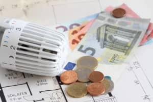 Nahaufnahme eines Heizkörperthermostats auf einem Wohnungsgrundriss mit Euro-Münzen und -Scheinen
