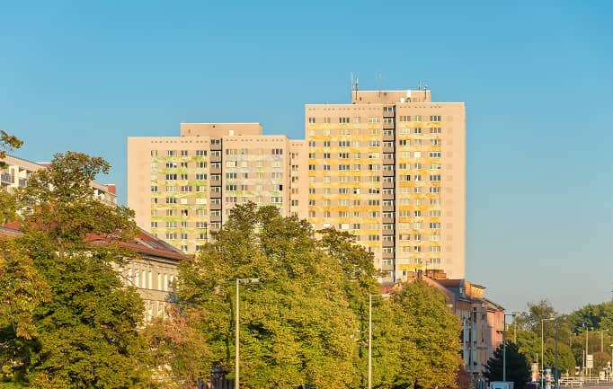 Вид на две высокие жилые башни с желто-зелеными акцентами на окнах за зелеными деревьями