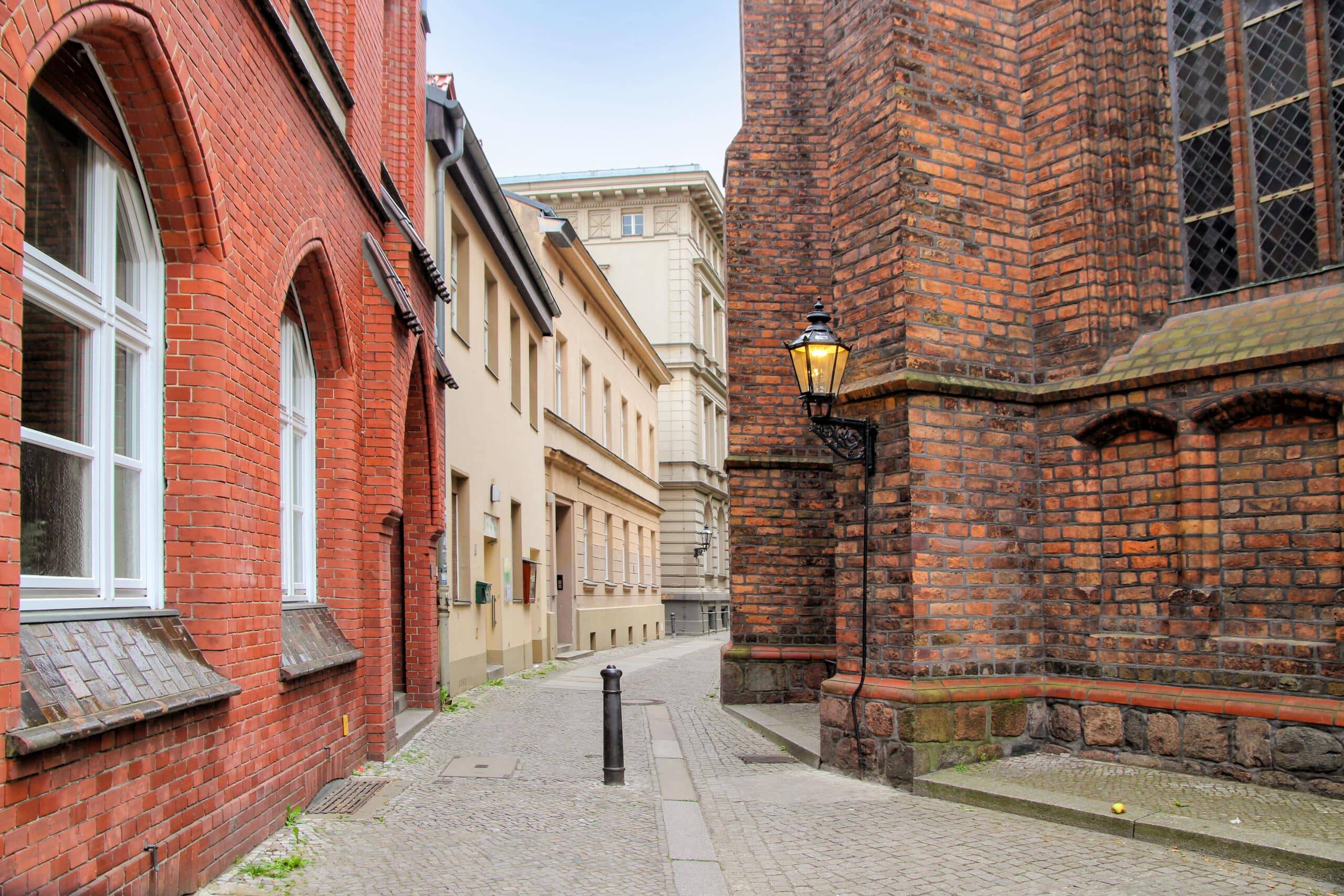schmale Kopfsteinpflastergasse zwischen roten Klinkerfassaden und beiger Putzfassade mit historischer Wandlaterne