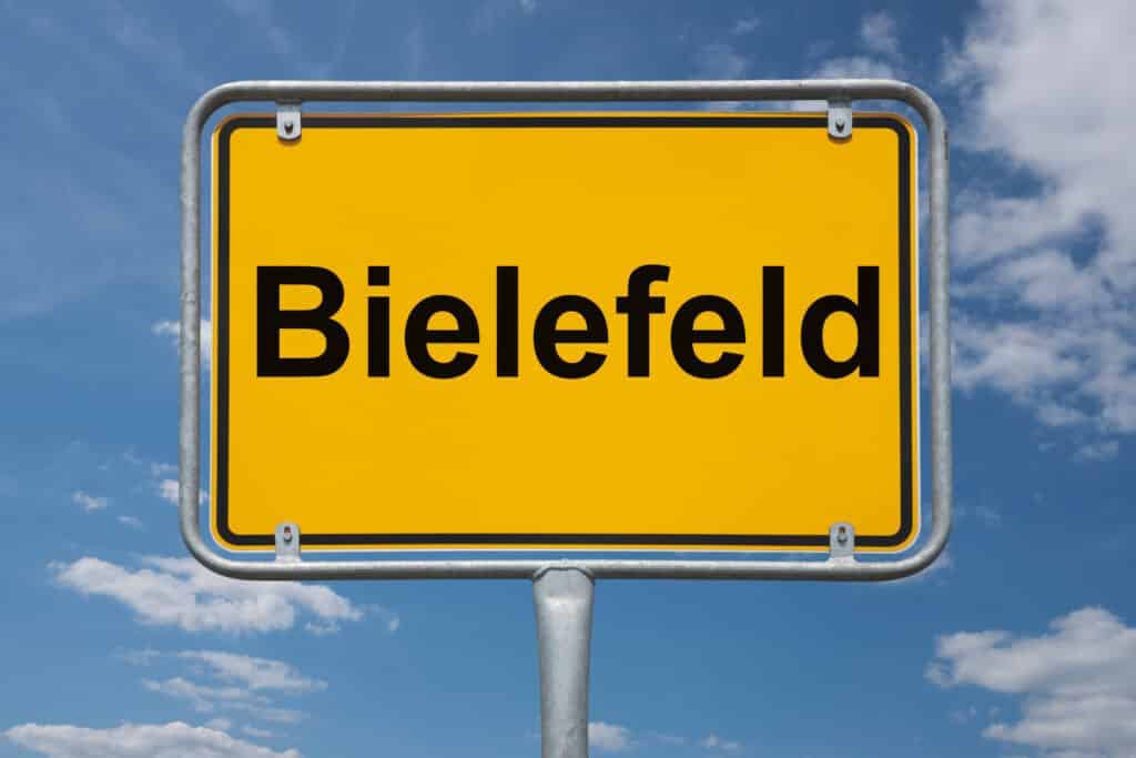 gelbes Ortseingangsschild mit Aufschrift Bielefeld frontal vor wolkenverziertem Himmel