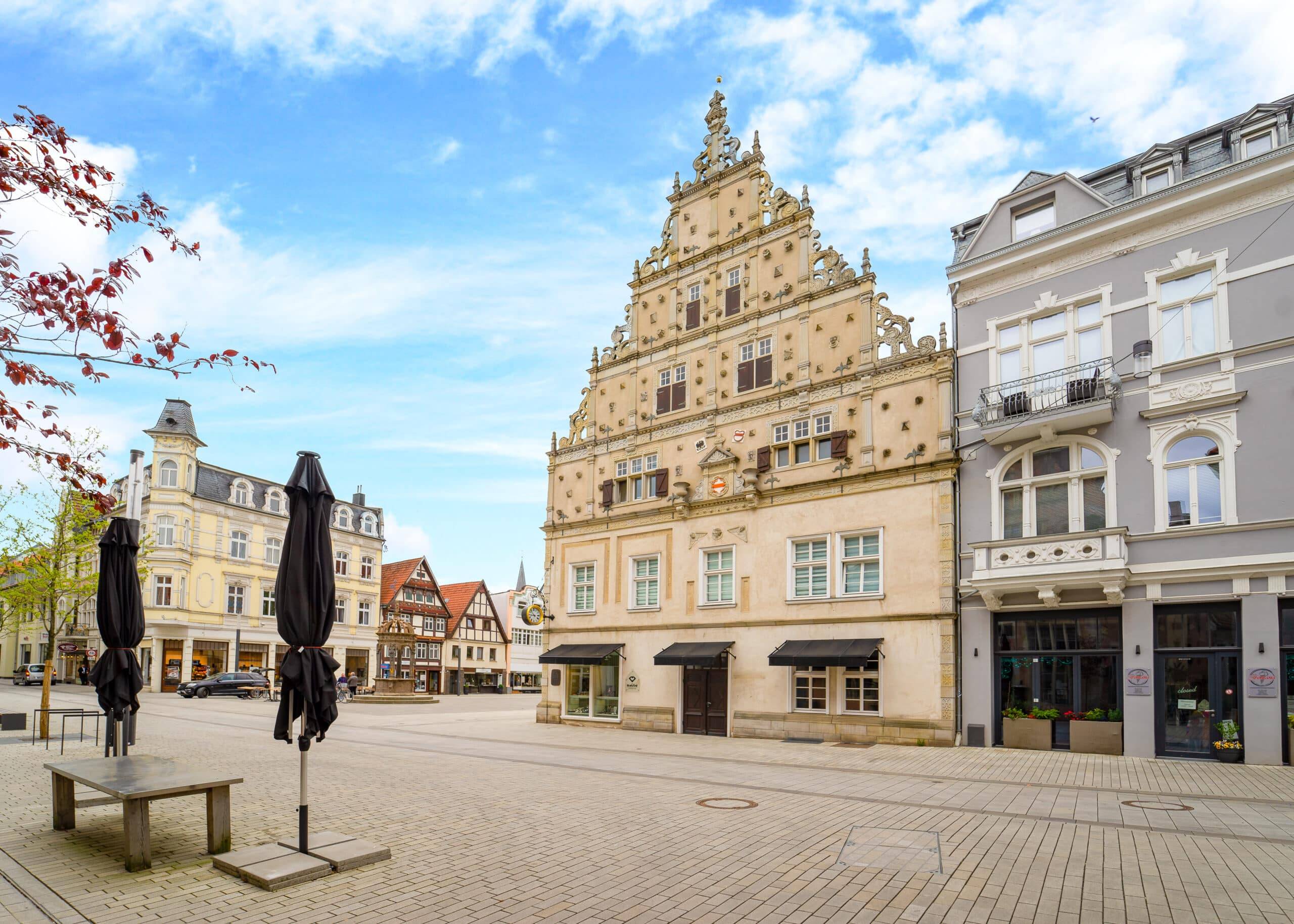 Historisches Stadthaus mit reich verziertem Treppengiebel von schräger Frontperspektive neben grauem Gebäude mit Balkon