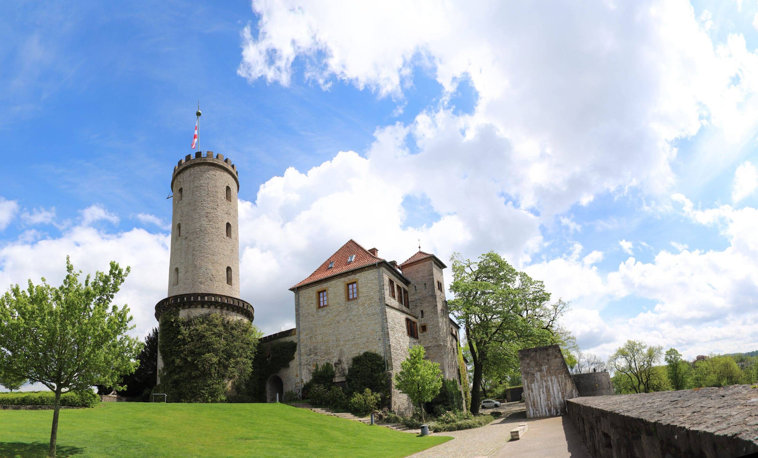 Steinerne Burg mit Rundturm und rotem Ziegeldach in Untersicht mit gepflegtem Rasen im Vordergrund