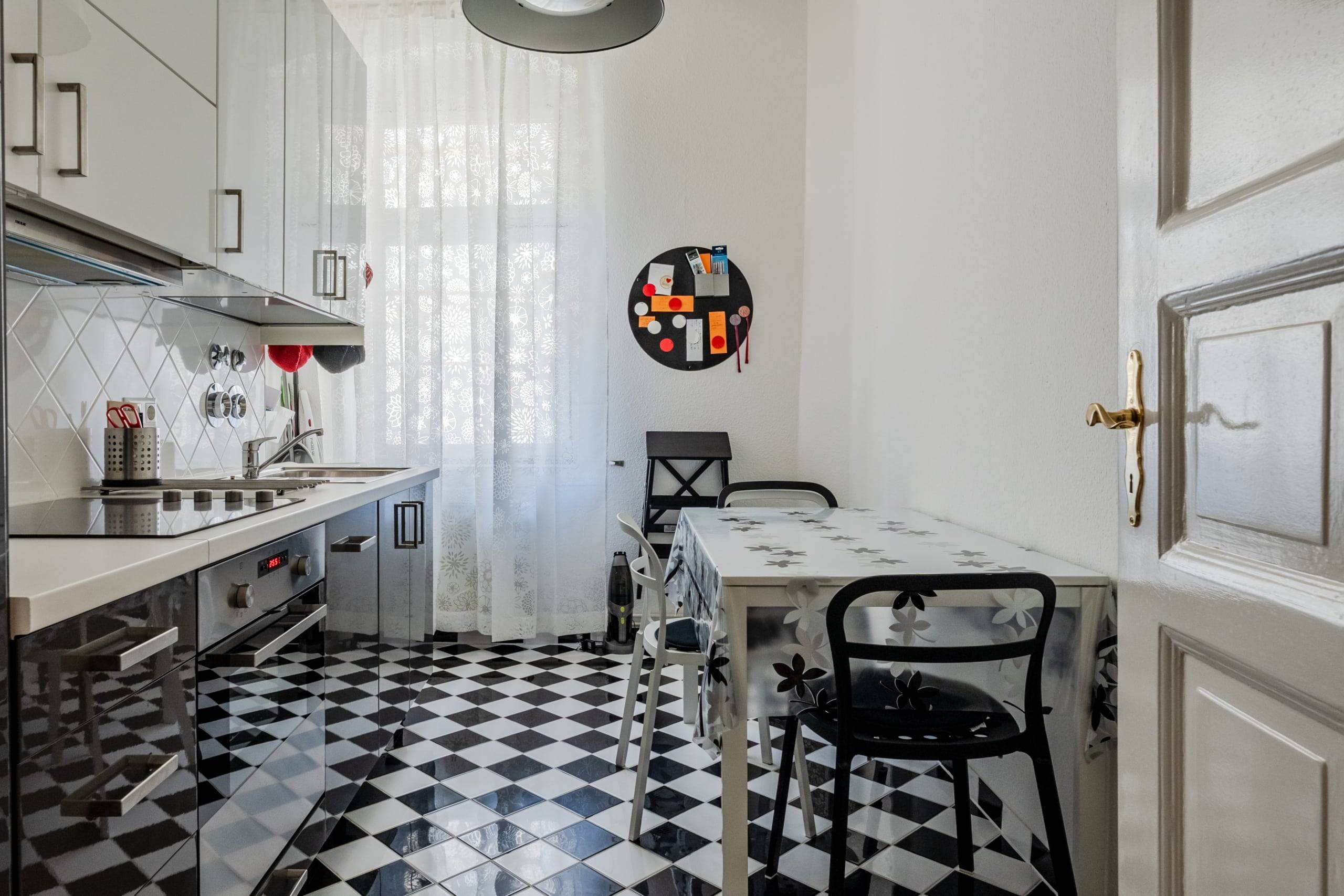 Vue intérieure d'une cuisine d'appartement moderne avec un sol en damier noir et blanc, des façades grises élégantes et une petite table à manger