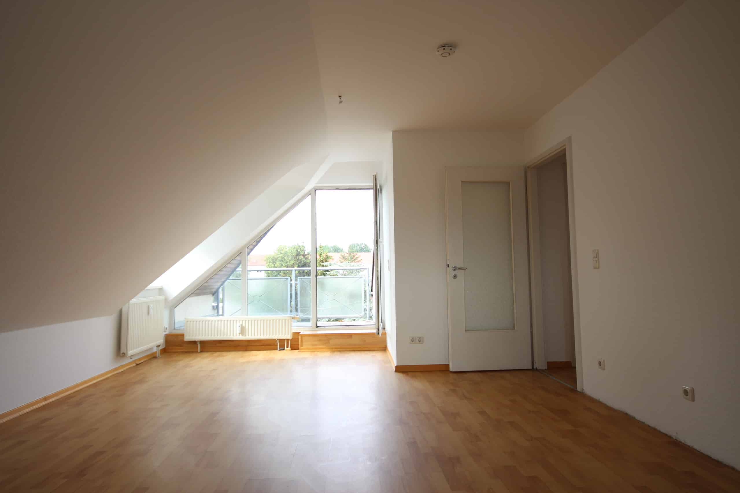Innenansicht einer Dachgeschosswohnung mit Parkettboden, Schräge und offenem Balkonfenster