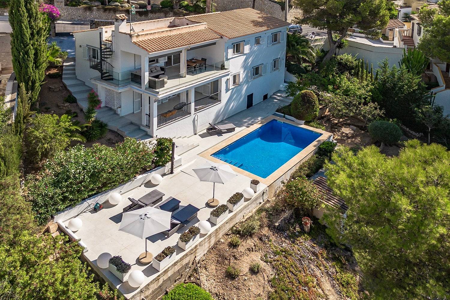 Vogelperspektive auf weiße mediterrane Villa mit Pool Panoramabalkon großer Terrasse Sonnenschirmen und Außentreppe