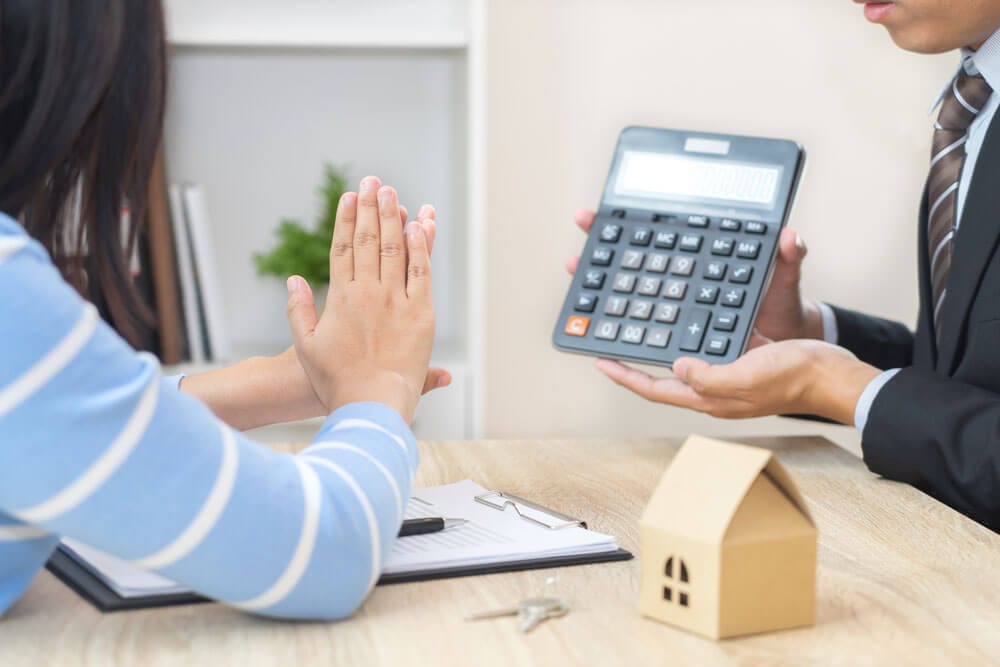 Tischperspektive auf Immobilienberatung mit Hausmodell Schlüssel und Taschenrechner