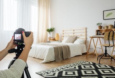Vista interna della camera da letto con letto matrimoniale davanti alla finestra, pavimento in legno, scrivania e piante