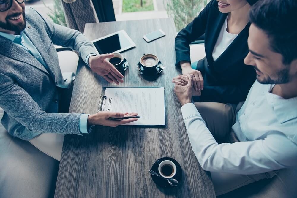 Contractondertekening voor de verkoop van een flat in vogelvlucht met houten tafel, koffiekopjes en tablet