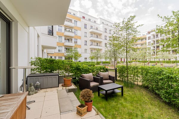 Appartement op de begane grond met terras en zitmeubilair op de lommerrijke binnenplaats van een modern appartementencomplex