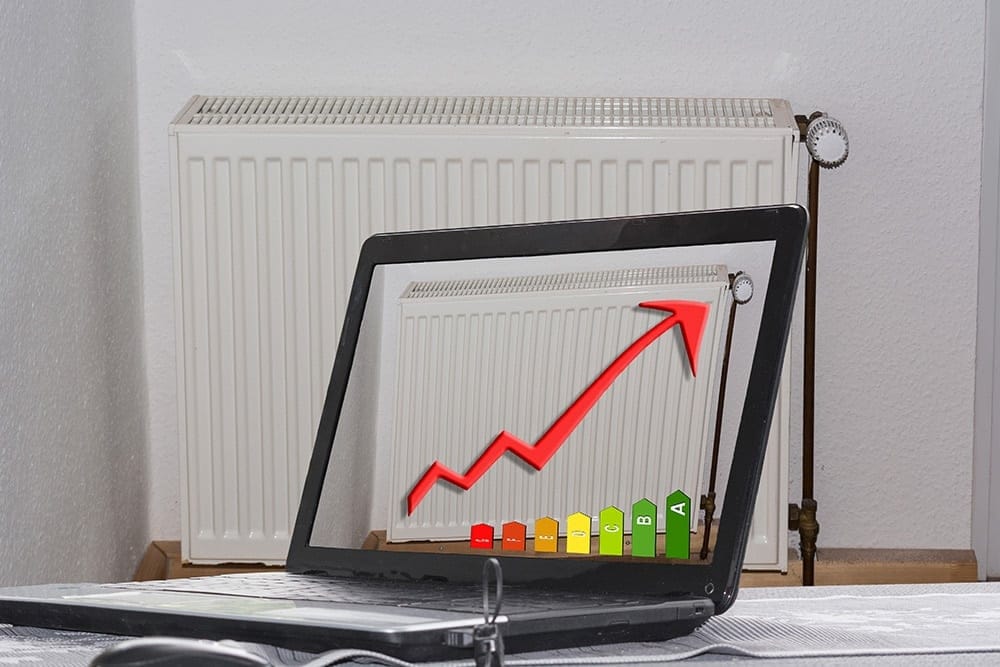 Vooraanzicht van een radiator voor een lichtgekleurde muur met open laptop en energie-efficiëntiediagram met rode pijl