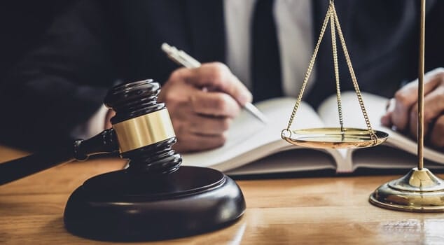 Nahaufnahme Richterhammer und Justitia-Waage vor aufgeschlagenem Gesetzbuch