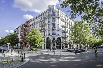 Вид на четырехэтажное угловое здание с белым фасадом и коваными балконами.