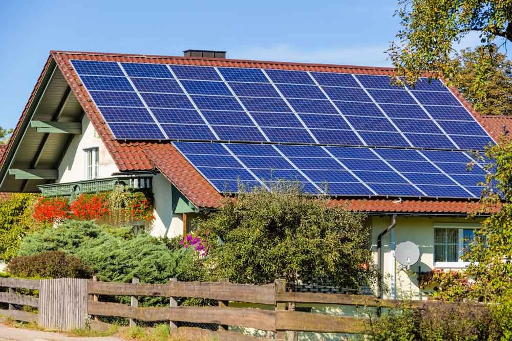 Vooraanzicht van een vrijstaand huis met schuin dak en grote zonnepanelen Balkon met bloemen en tuinhek