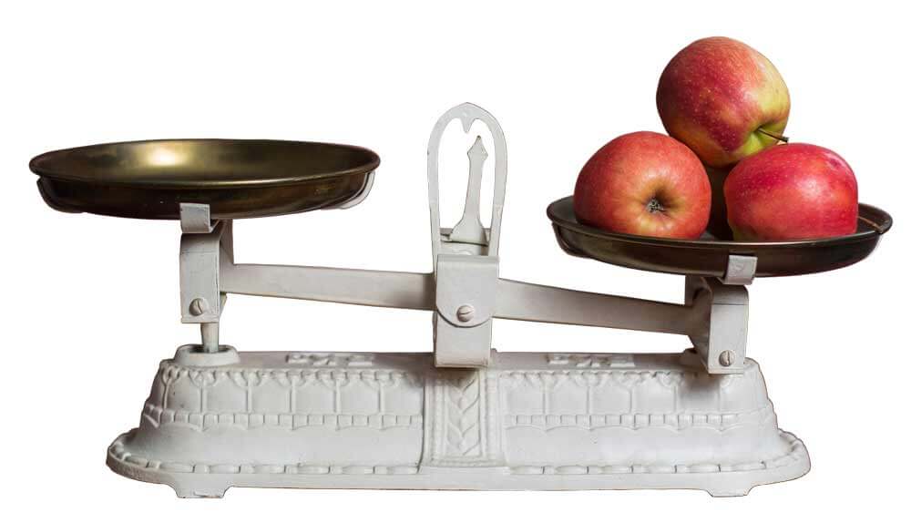 Antique scales with three red apples on the right bowl, left bowl empty, side view