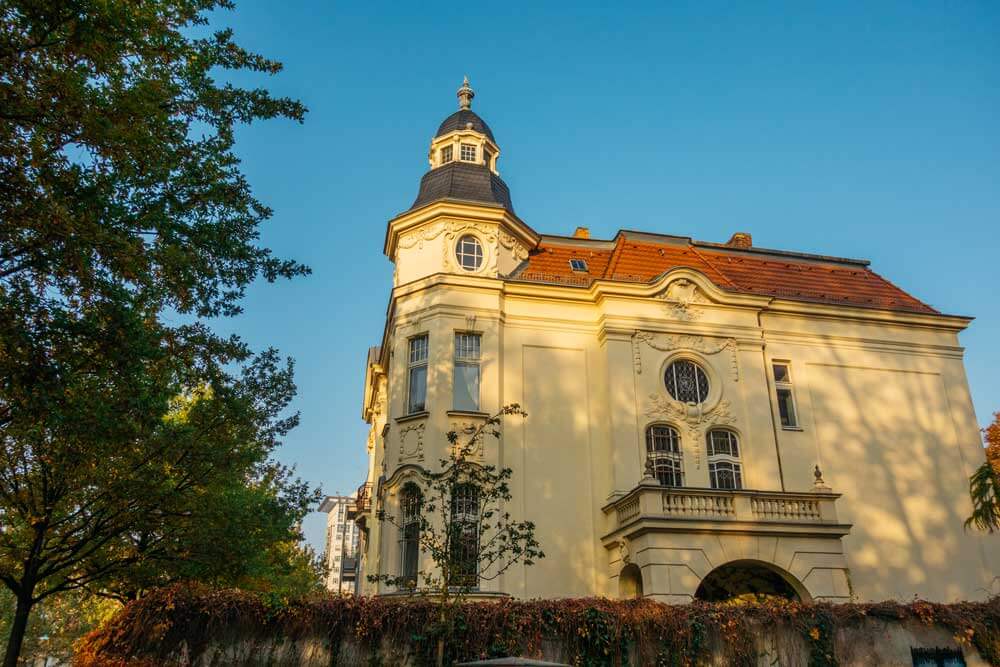 Historische Stadthausvilla in Frontansicht mit Turmkuppel, Erker, verzierten Stuckfassade und roten Dachziegeln