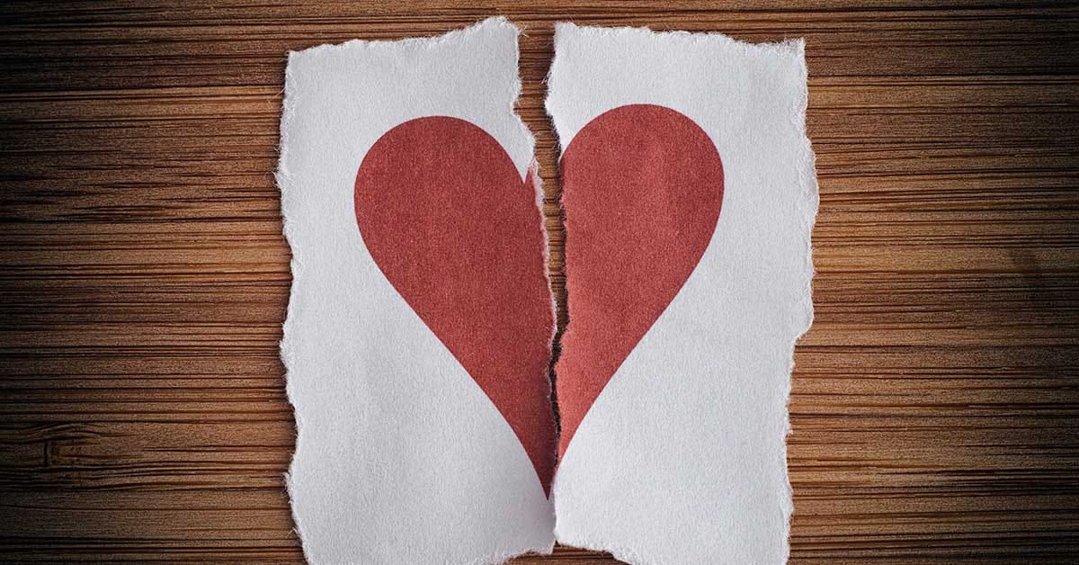 torn red heart on two pieces of paper in front of a wooden background