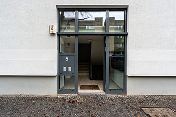 Frontalansicht Mehrfamilienhauseingang Nr 5 mit Glas-Stahltür Seitenelementen vor heller Putzfassade