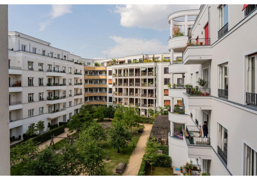 Innenhof eines fünfgeschossigen weißen Mehrfamilienhauses mit Balkonen und begrüntem Garten aus erhöhter Perspektive