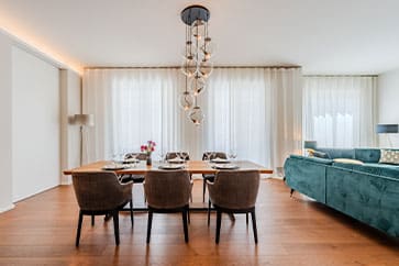 Blick auf modernen Wohn-Essbereich einer Neubauwohnung mit Holzdielen Esstisch für sechs Designer-Hängelampe und Samtsofa