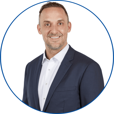 一位身着深色西装、面带微笑的男子的肖像照，白色背景，蓝色边框的圆圈内