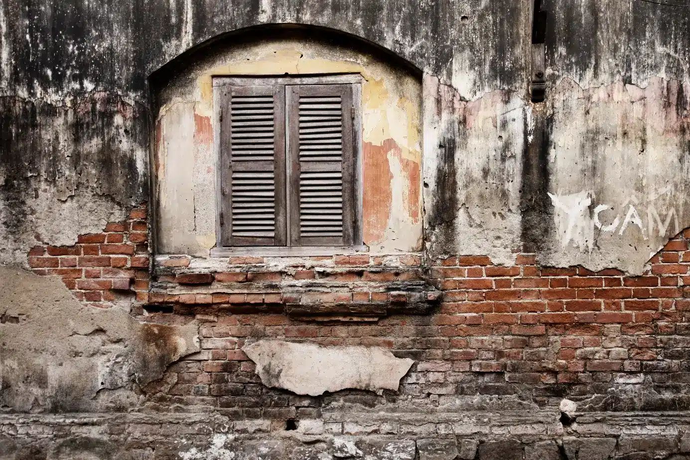 Front view of dilapidated brick and plaster façade with closed wooden shutter window