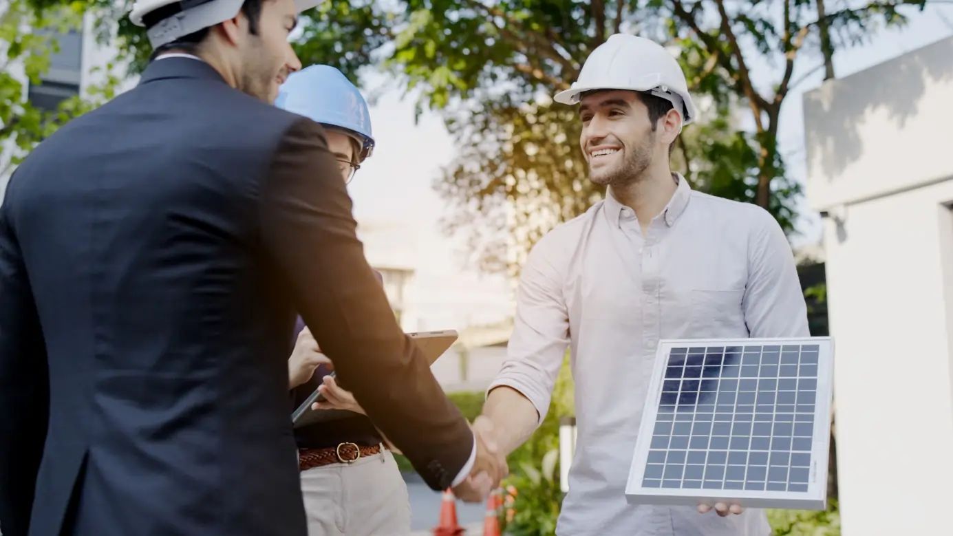 Handschlag mit Solarmodul in Außenansicht vor modernem Wohngebäude