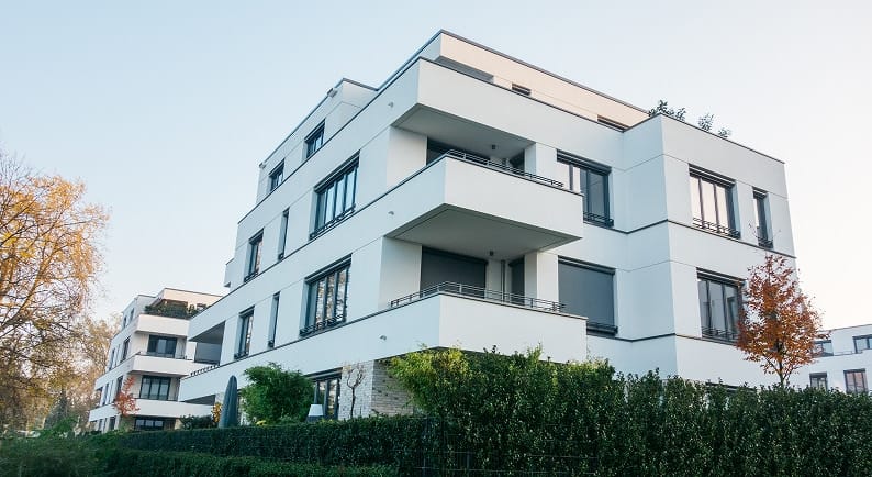 Straßenseitige Ecke eines weißen modernen Mehrfamilienhauses mit Balkonen Flachdach und Heckenbegrünung