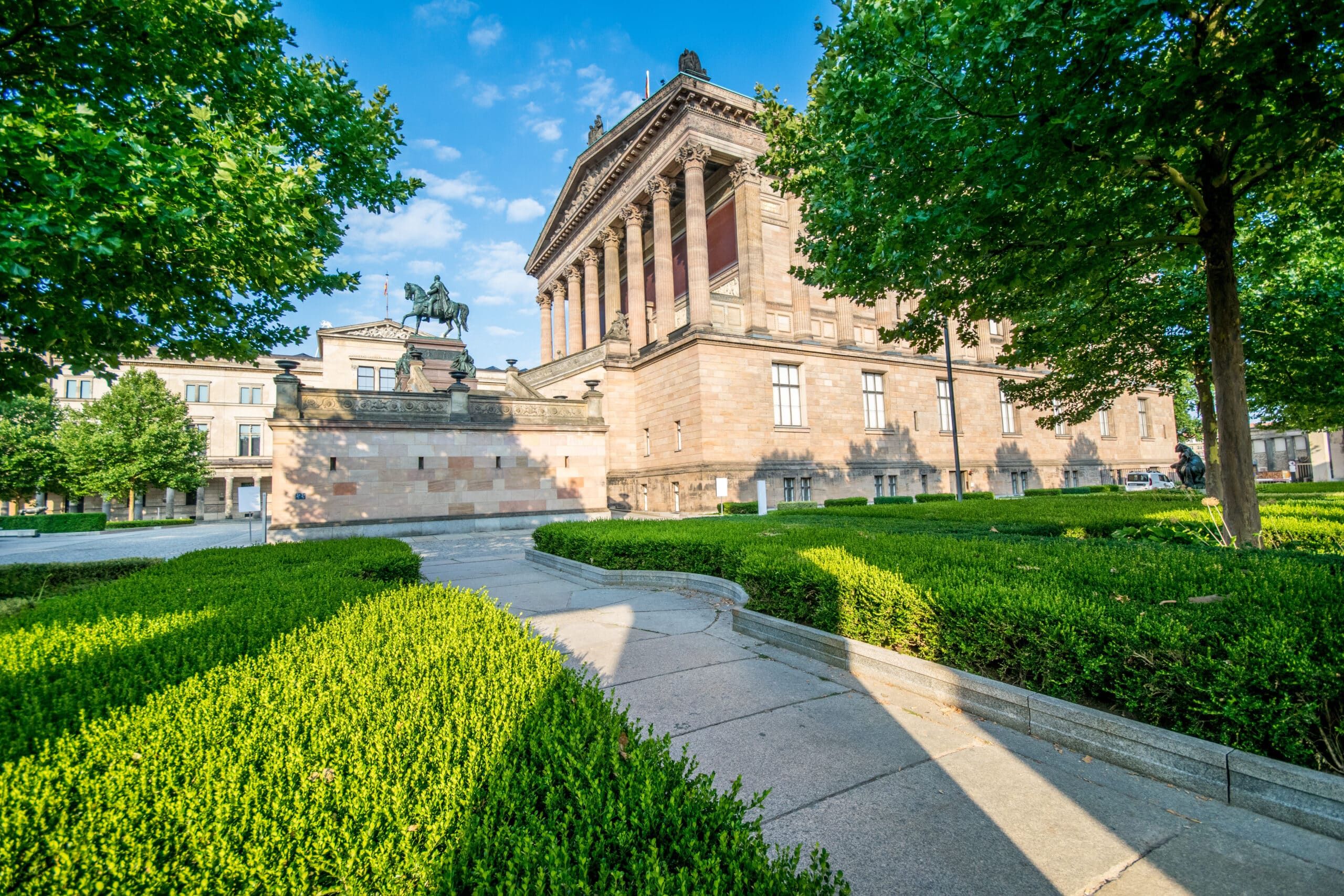 Historische neoklassizistische Fassade mit Säulenfront, seitlicher Blick auf Reiterstandbild und formelle Buchsbaumgärten