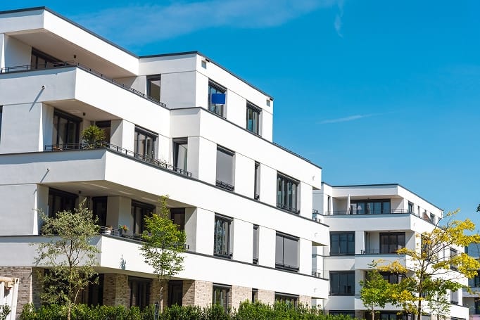 Белый современный жилой дом с балконами, клинкерным цоколем и большими окнами с угловой фронтальной перспективы