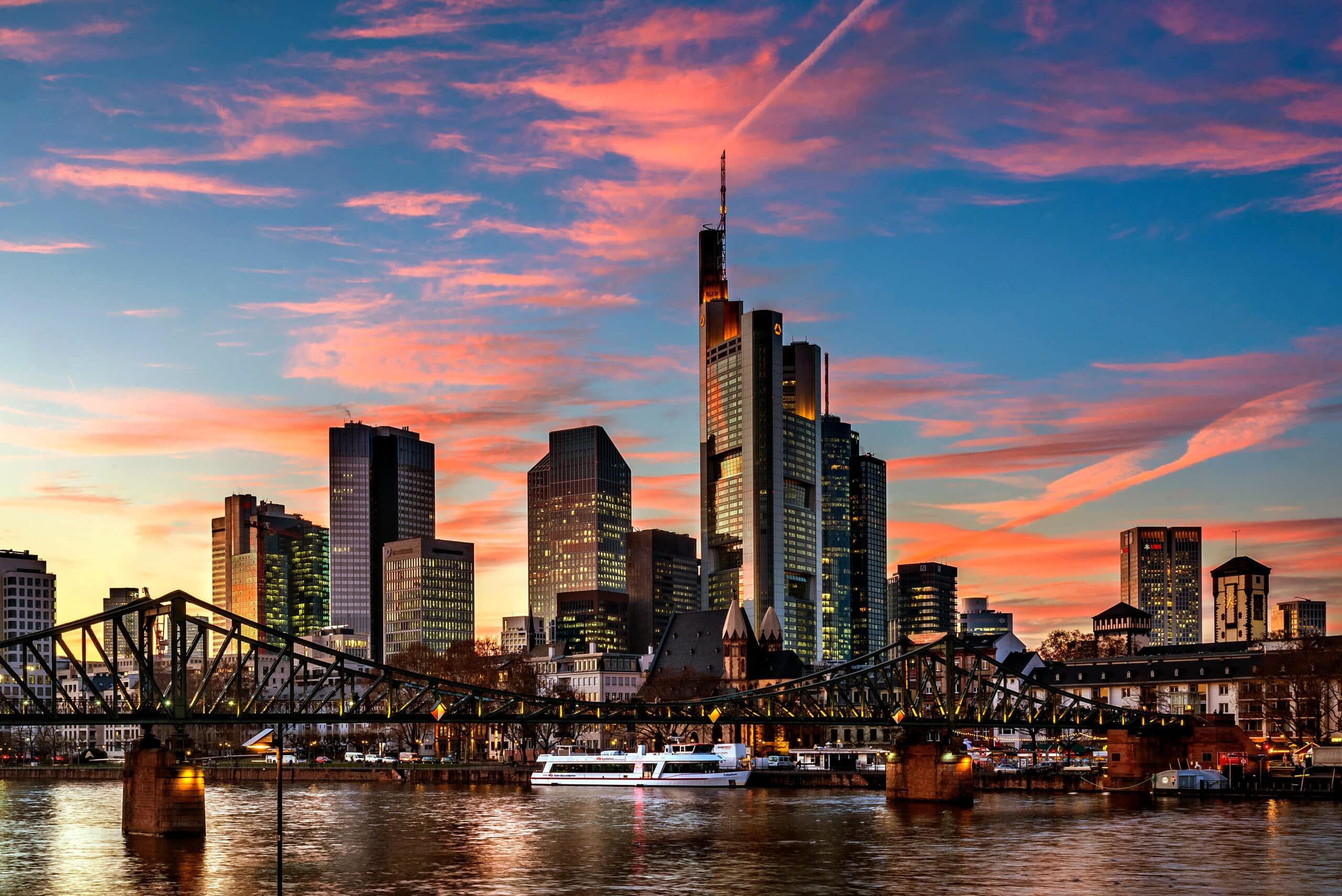 Panoramablick auf Frankfurter Skyline mit Bürohochhäusern und Stahlbrücke über den Main bei Abendrot