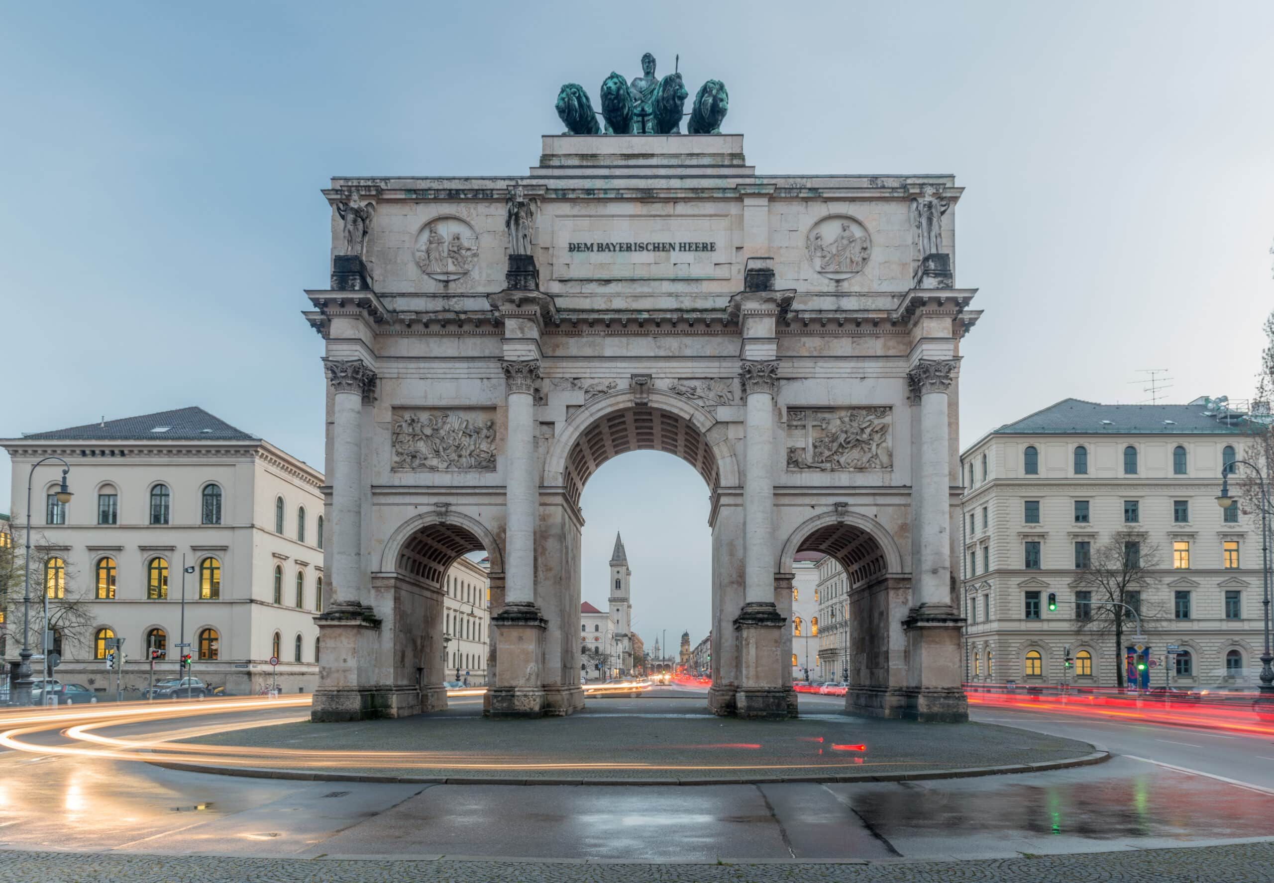 historischer Triumphbogen in Zentralperspektive mit drei Torbögen und Quadriga auf Sandsteinfassade umgeben von Stadthäusern