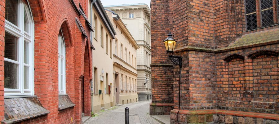 Smalle steeg met kinderkopjes tussen rode bakstenen gevels en beige pleistergevel met historische muurlantaarn