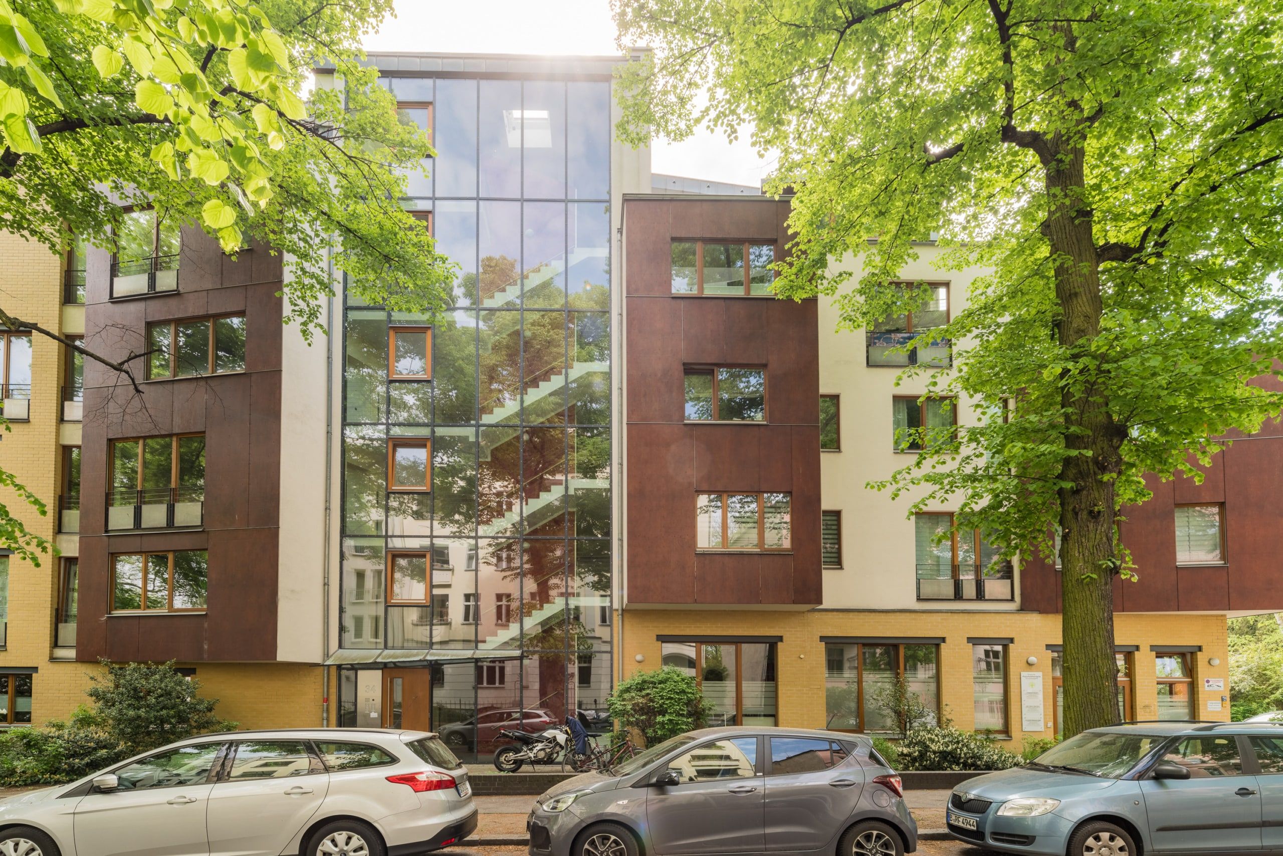 Mehrfamilienhaus frontalansicht mit zentraler Glasfassade Treppenhaus rote Metallfassade und begrünter Vorgarten