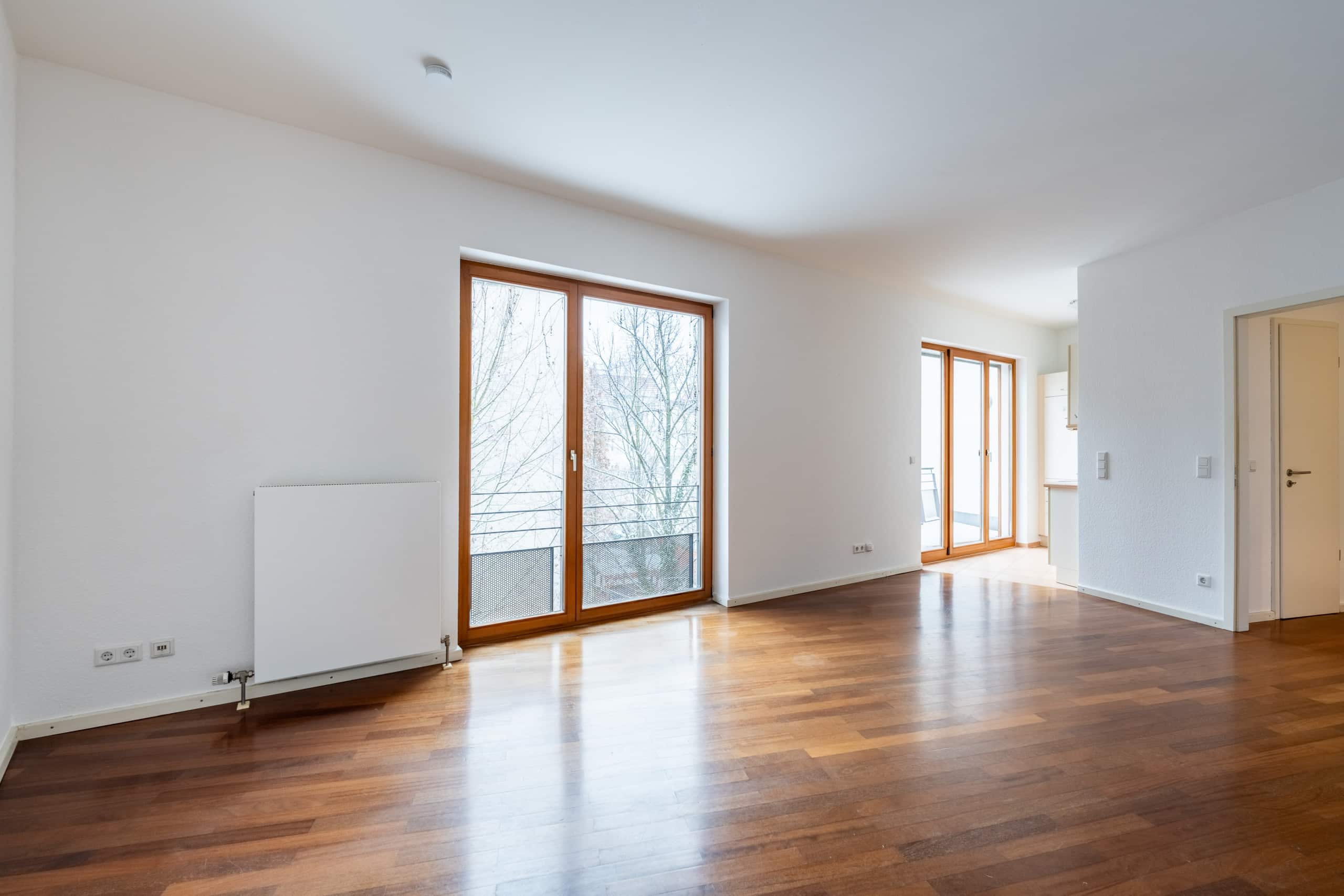 Heller leerer Wohnraum mit Parkettboden und bodentiefen Holz-Terrassentüren mit französischem Balkon