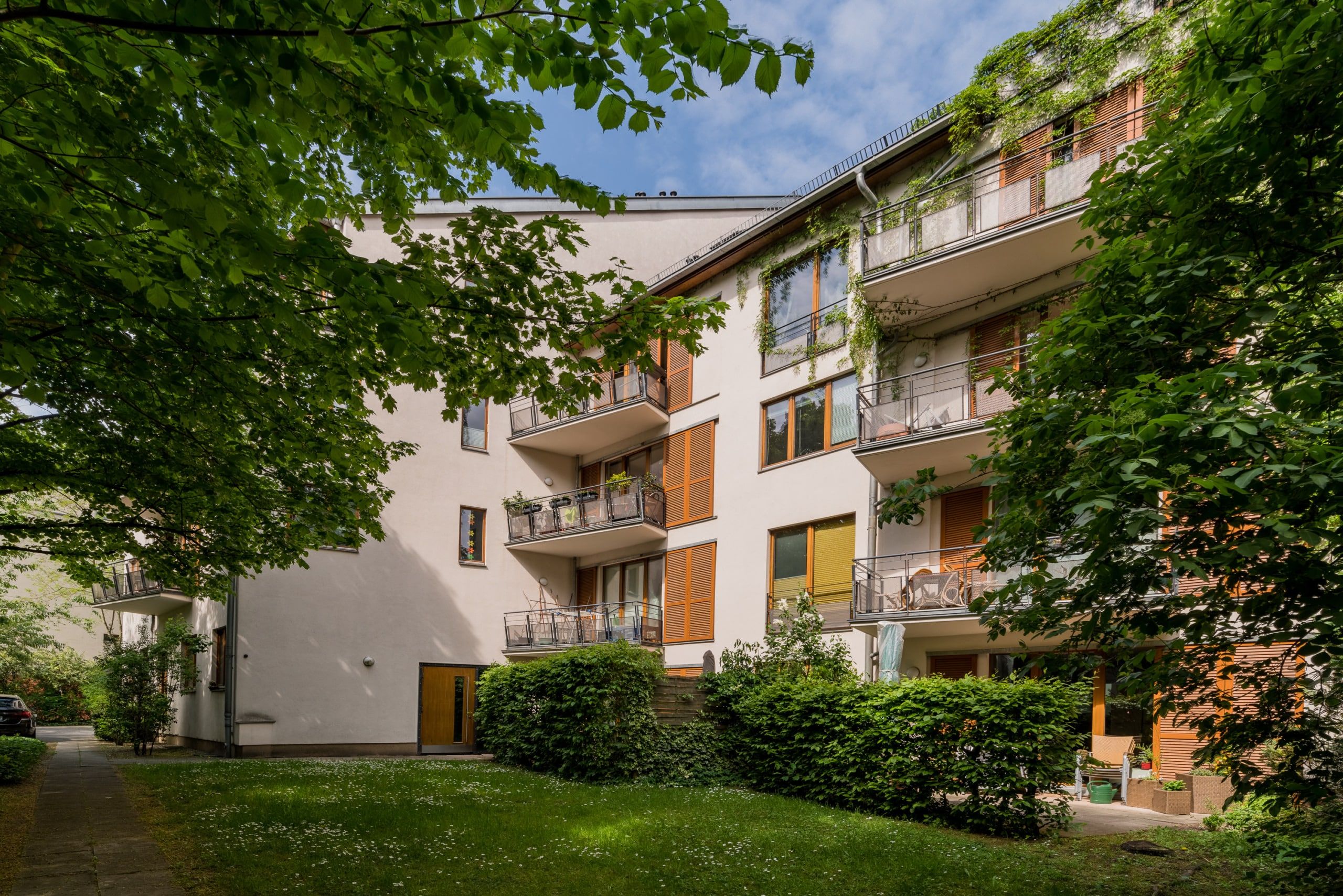 Mehrfamilienhaus mit drei Etagen Hofansicht weisse Putzfassade Holzläden Balkone und grüner Innenhof