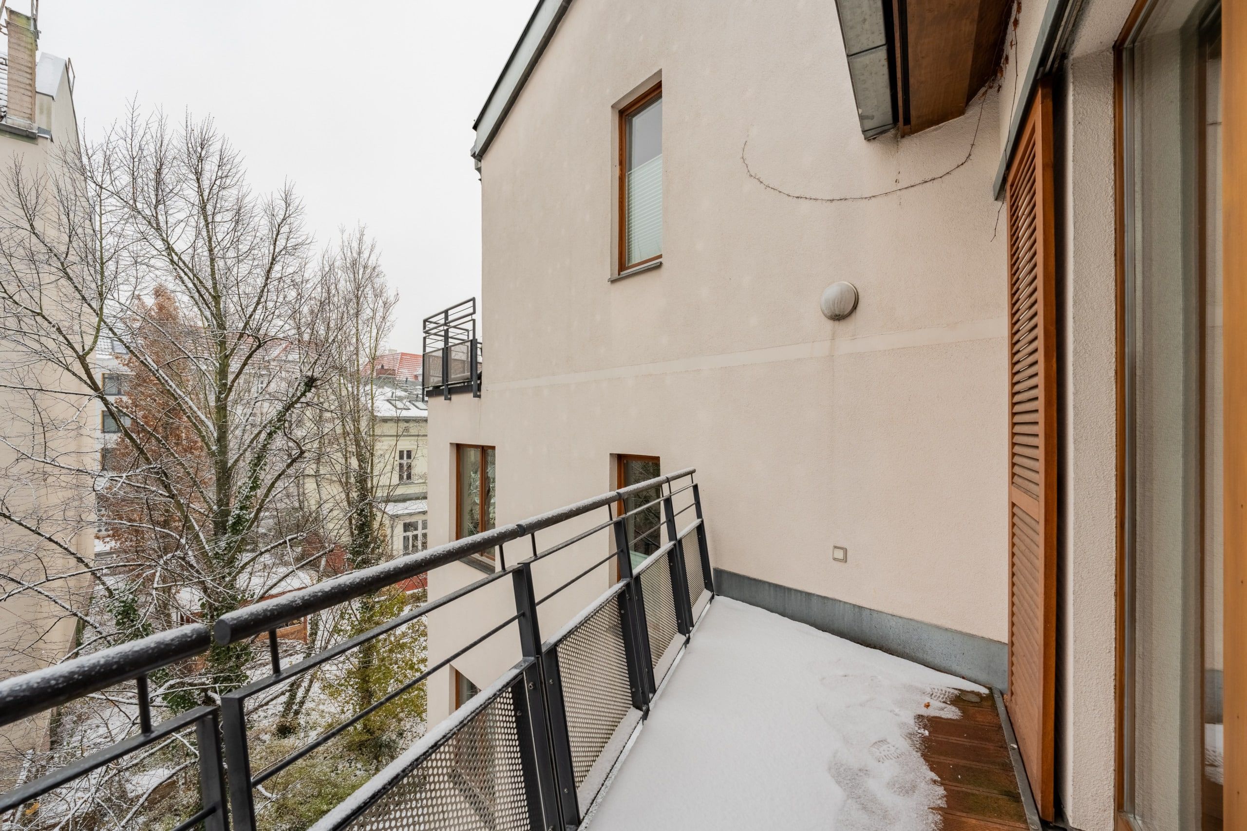 Balkon einer Mehrfamilienwohnung mit Metallgeländer und Schneeablagerung Blick auf benachbarte Gebäude und Winterbäume