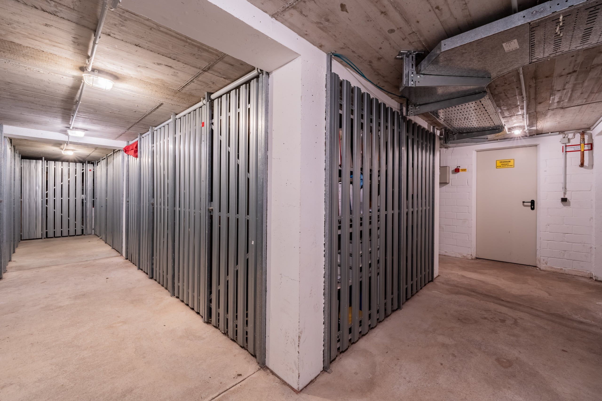 Kellerflur mit begehbarem Abstellbereich aus Metallgitter und weißer Technikraumtür