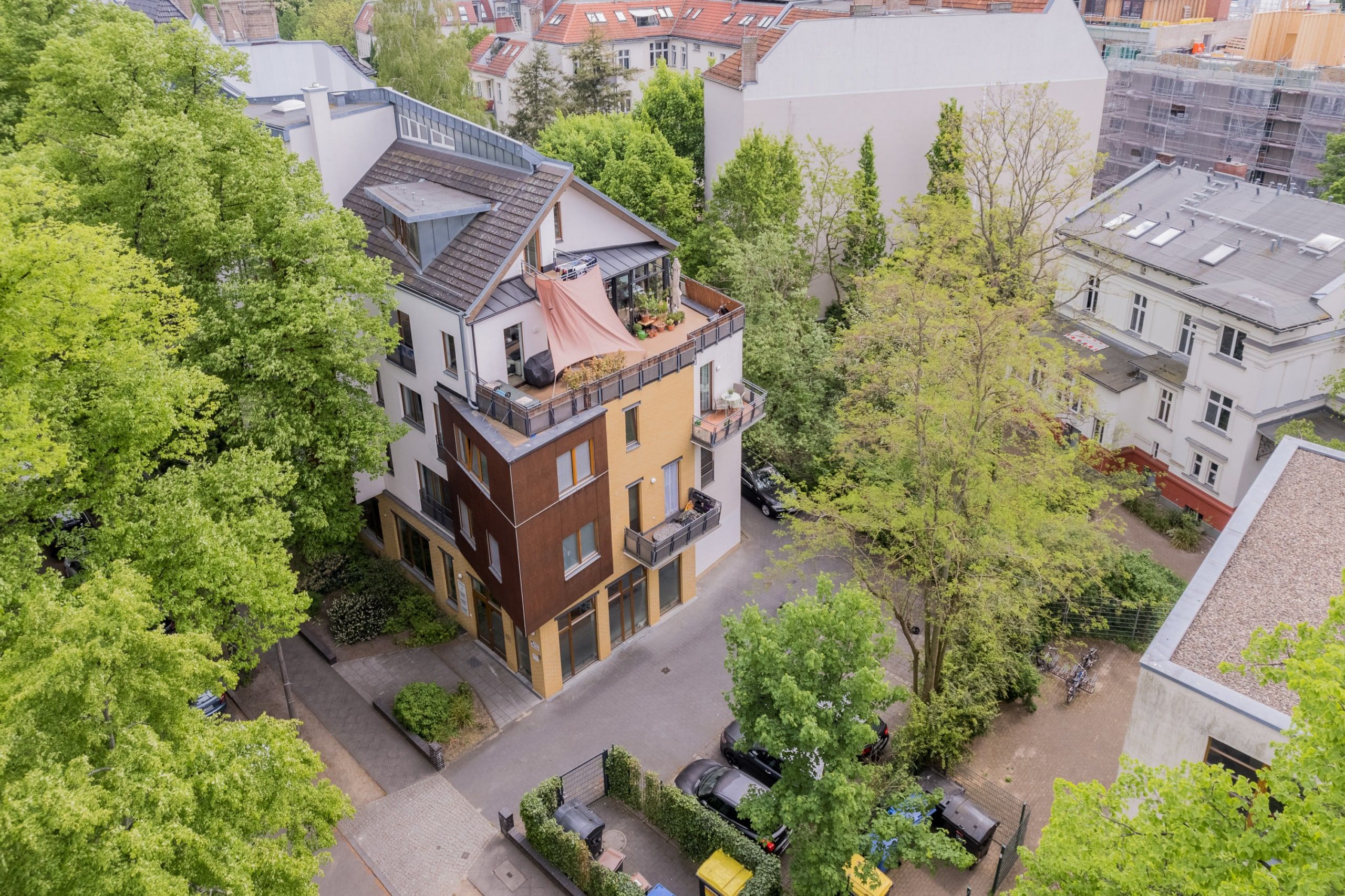 Vogelperspektive auf modernes mehrgeschossiges Stadthaus mit Dachterrasse und Balkonen umgeben von Bäumen