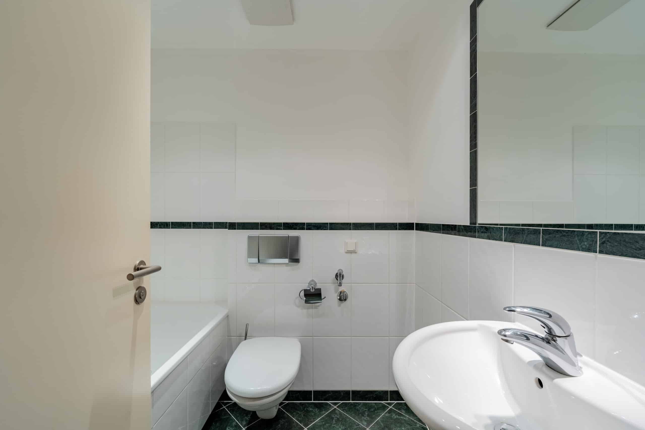 Innenaufnahme Badezimmer mit wandhängendem WC Eckbadewanne Waschbecken Spiegel und grünen Bordüren- und Bodenfliesen