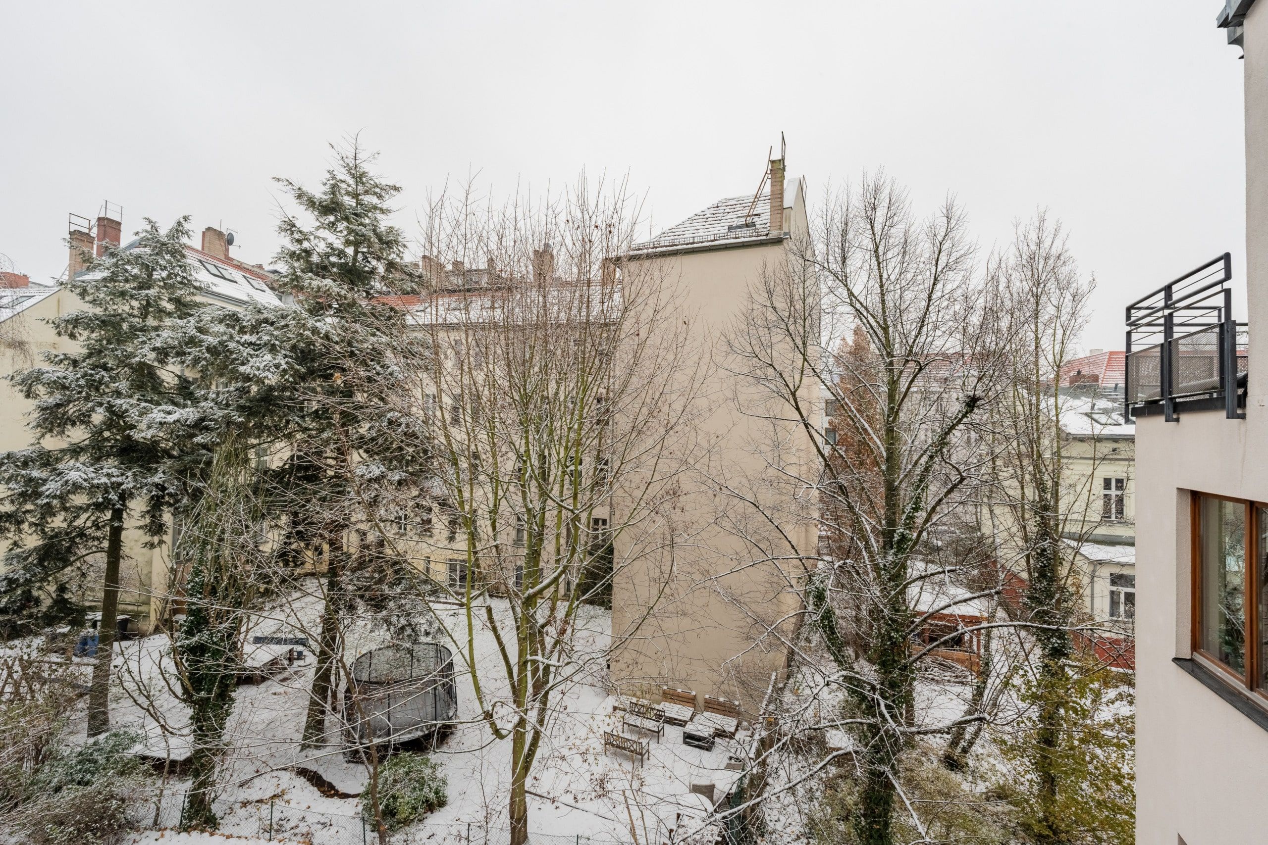 Innenhofansicht eines mehrstöckigen Wohnhauses mit verschneitem Gartenbereich Sitzbänken unbelaubten Bäumen und Balkon