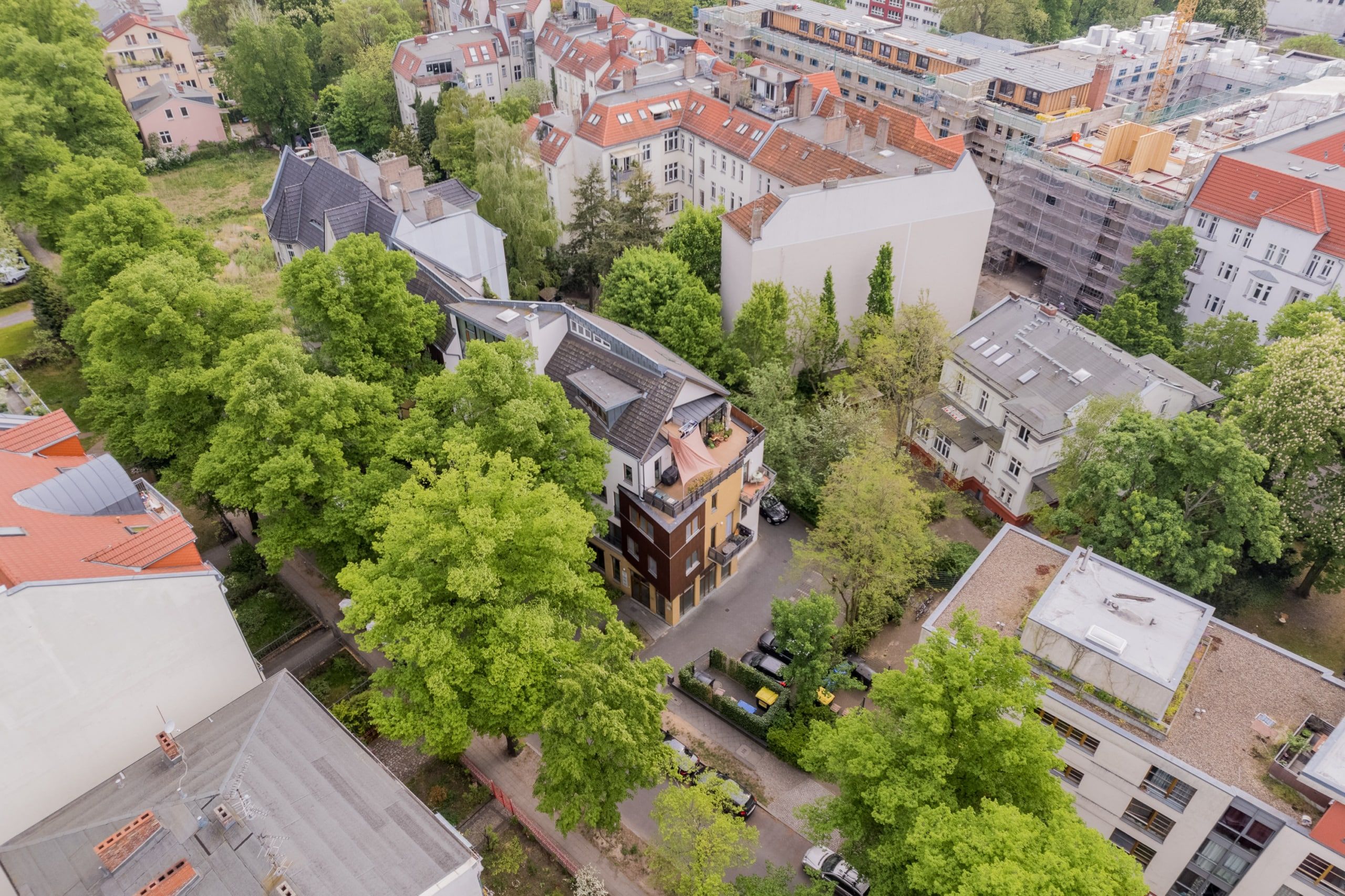 Draufsicht auf modernes Mehrfamilienhaus mit Penthouse-Terrasse, begrüntem Innenhof und umliegendem Baumbestand